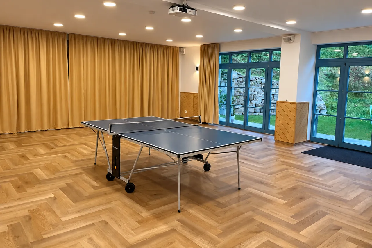 Tělocvična se stolem na stolní tenis, parketami a prosklenými dveřmi na zahradu