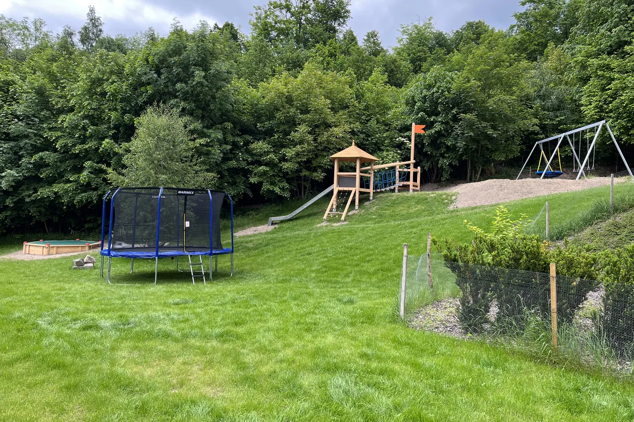 Zahrada hotelu pod lesem s trampolínou, dětským hřištěm a houpačkami